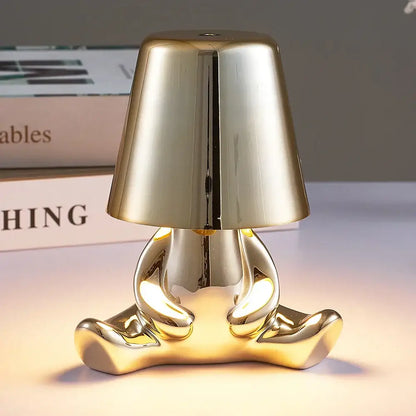 Golden glossy ceramic man table lamp shaped like a seated figure with bell-shaped shade for bedroom night light