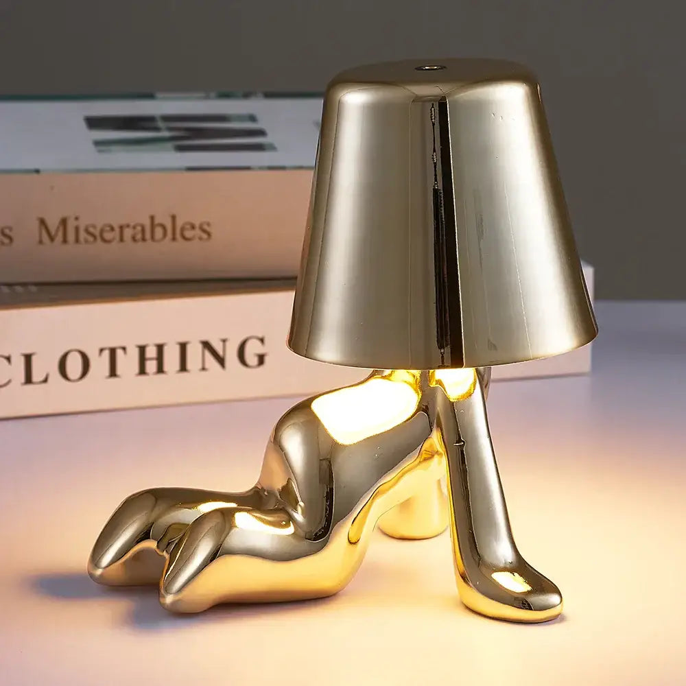 Gold-colored glossy metallic articulated man table lamp shaped like a reclining shoe with inverted conical shade night light