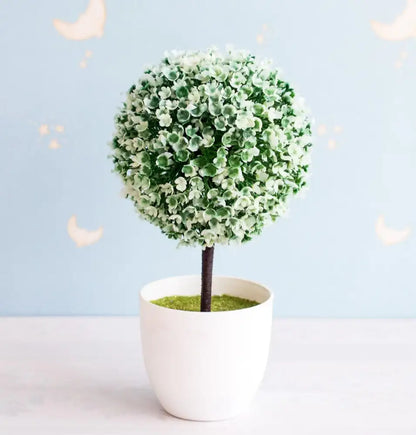 A round artificial bonsai tree with dense green and white blossoms in a white ceramic pot for garden decor
