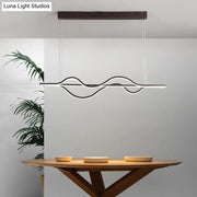 Modern black and white artistic metal dining pendant light fixture with wavy design hanging above wooden table