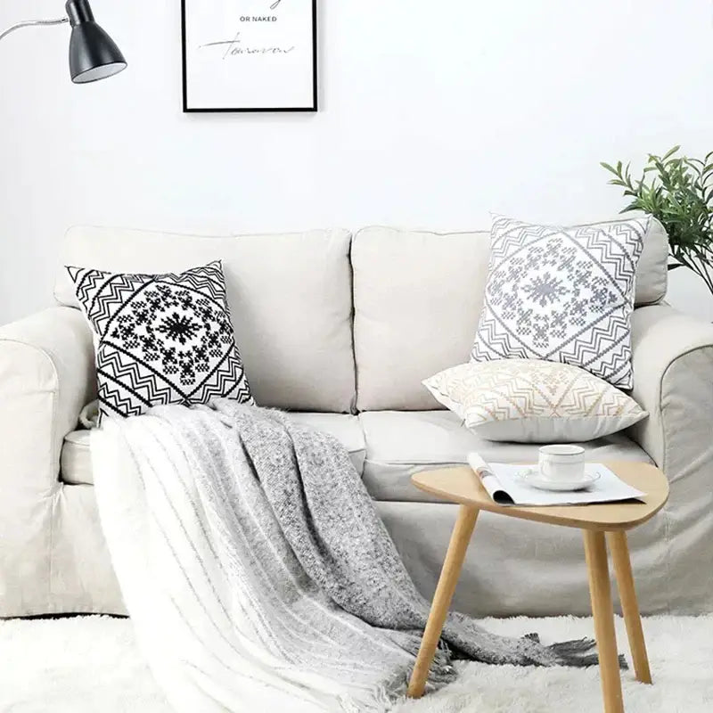 Beige upholstered sofa with three black and white geometric aztec embroidery canvas cushion covers and gray throw blanket