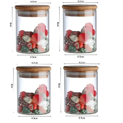 Clear glass food storage jars with bamboo lids holding colorful candies labeled for kitchen spice use