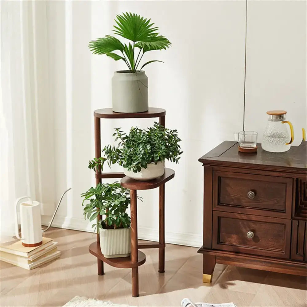 Dark wood bamboo tall corner plant stand with three circular shelves and slender legs holding green plants in ceramic pots