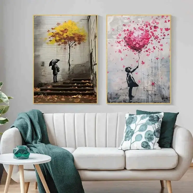 Two banksy boy girl balloon canvas prints in black frames hang above a white sofa with yellow and pink accents