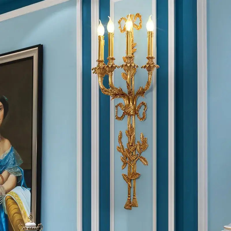 Golden ornate baroque antique brass wall sconce with three candle-style bulbs and leafy ribbon decorbites design