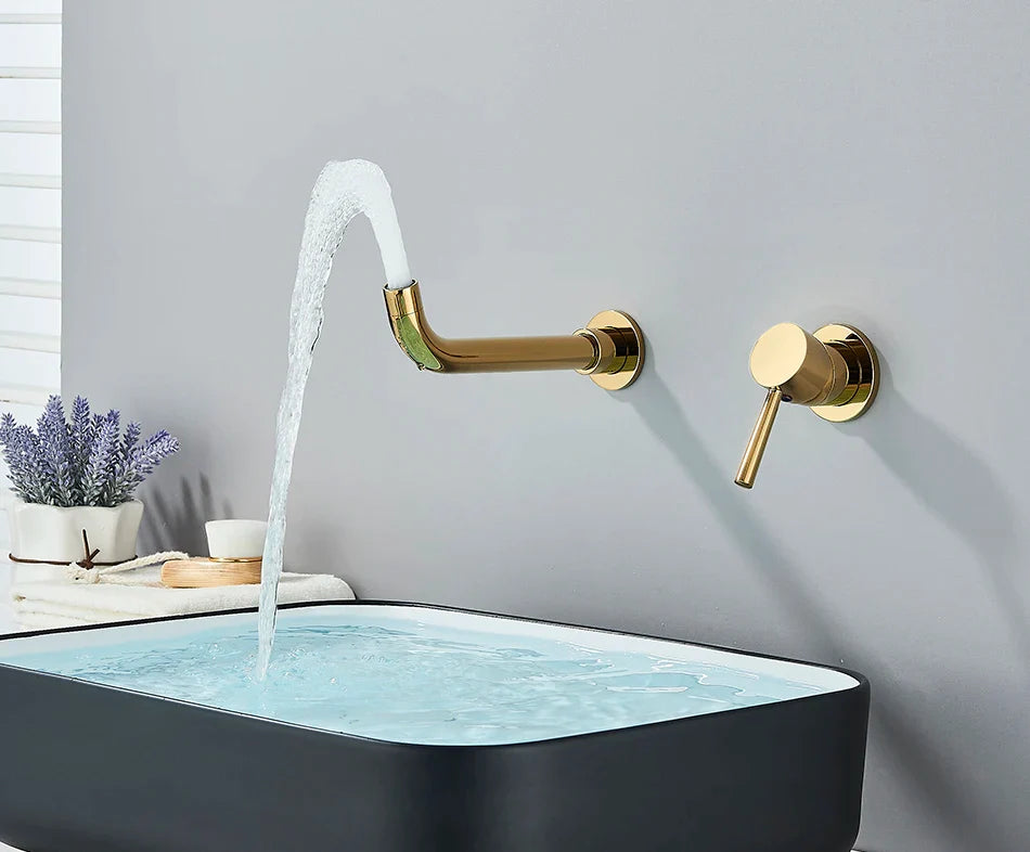 Gold-toned basin faucet wall mounted bathroom fixture with brushed brass finish and hot water control flowing cold hot water