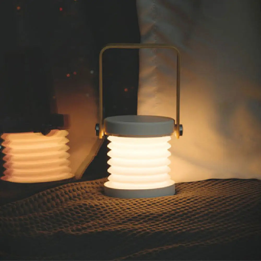 A sleek gray silicone collapsible wall sconce lantern with a soft white glow in a battery-operated design