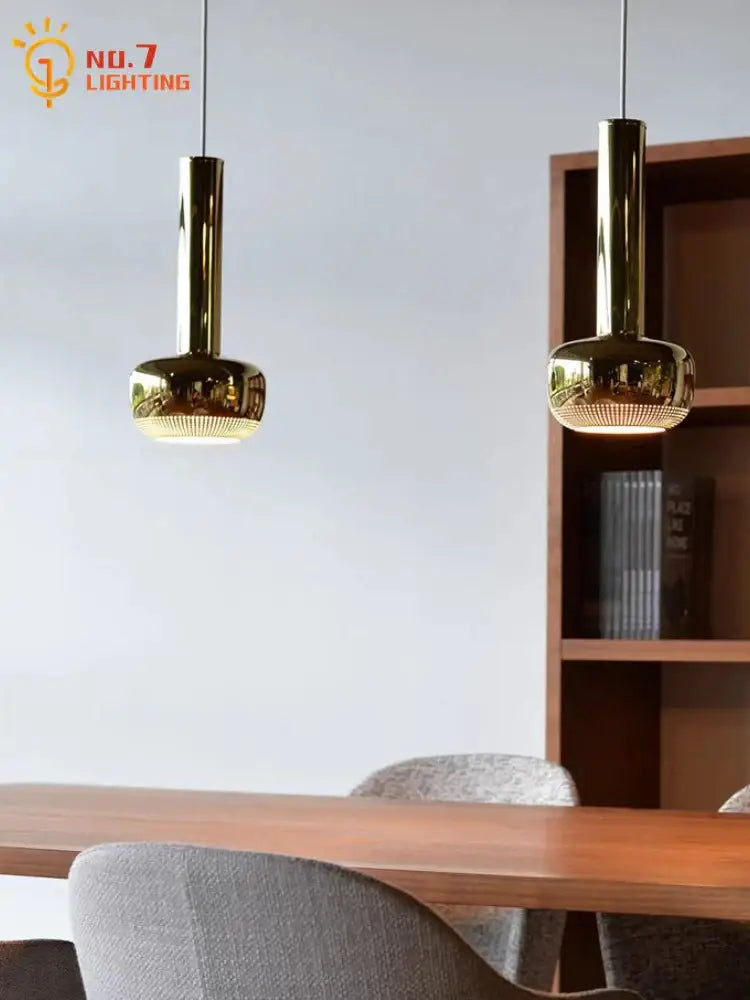 Two sleek gold bauhaus copper chrome pendant lights with cylindrical stems hang above a wooden kitchen island table