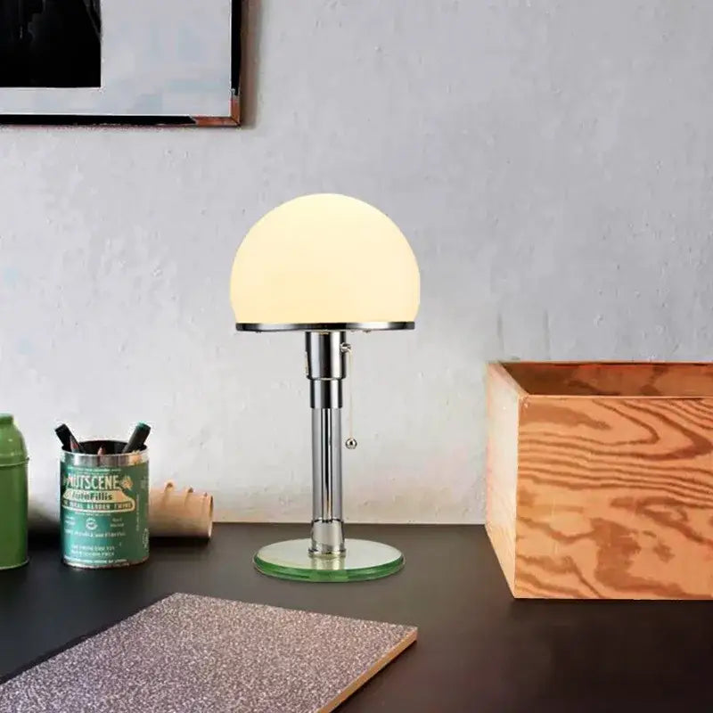A bauhaus mushroom table lamp with a frosted milk white glass dome and polished chrome stem for bedroom lighting
