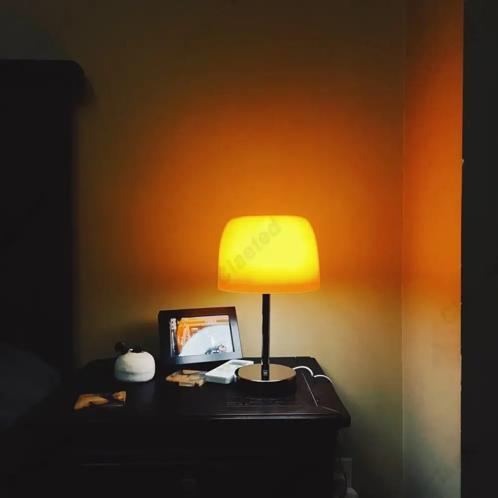 Warm yellow-glowing bauhaus orange glass retro table lamp with a chrome base and sleek black stem for bedroom use