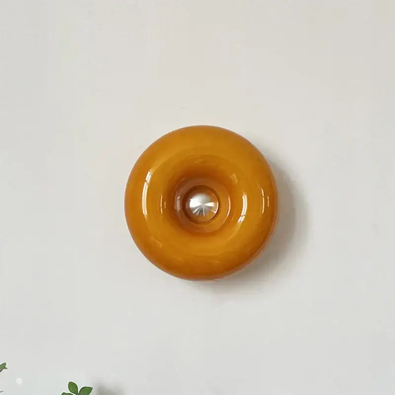 A bauhaus orange glass style glossy amber glass wall sconce with a central metallic accent for bedroom decor