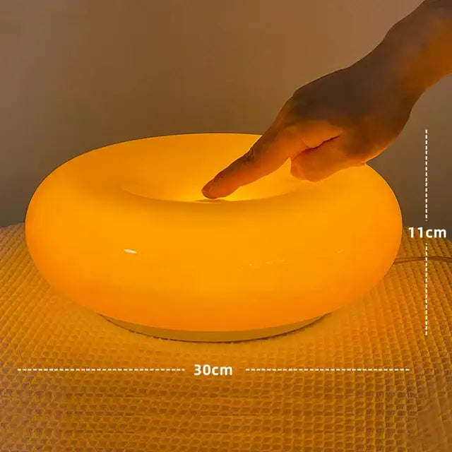 A bauhaus orange glass table lamp with a glowing smooth circular design and warm light for bedroom use