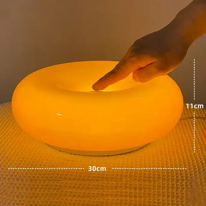 A bauhaus orange glass table lamp with a glowing smooth circular design and warm light for bedroom use