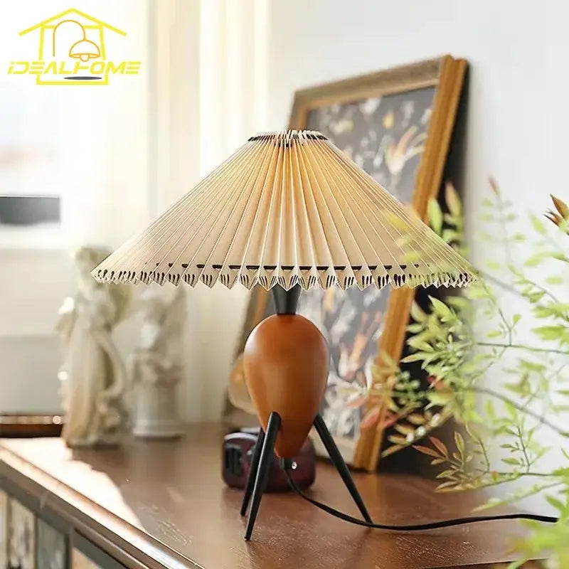 A bauhaus pleated wood table lamp with a warm-toned wooden base beige pleated paper shade and black tripod legs
