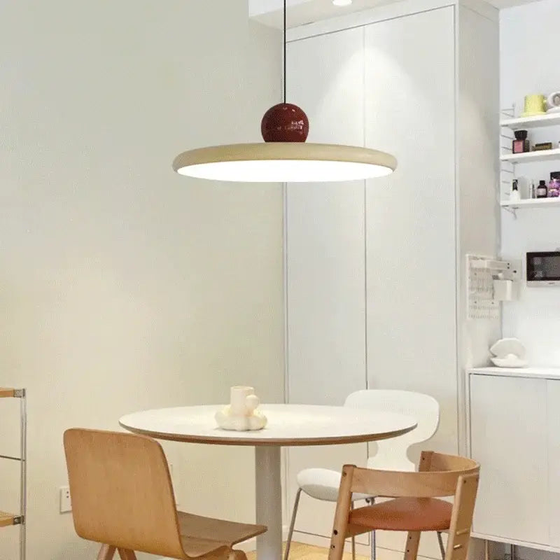 A bauhaus saucer chandelier with a circular matte white shade and glossy red spherical accent for dining rooms