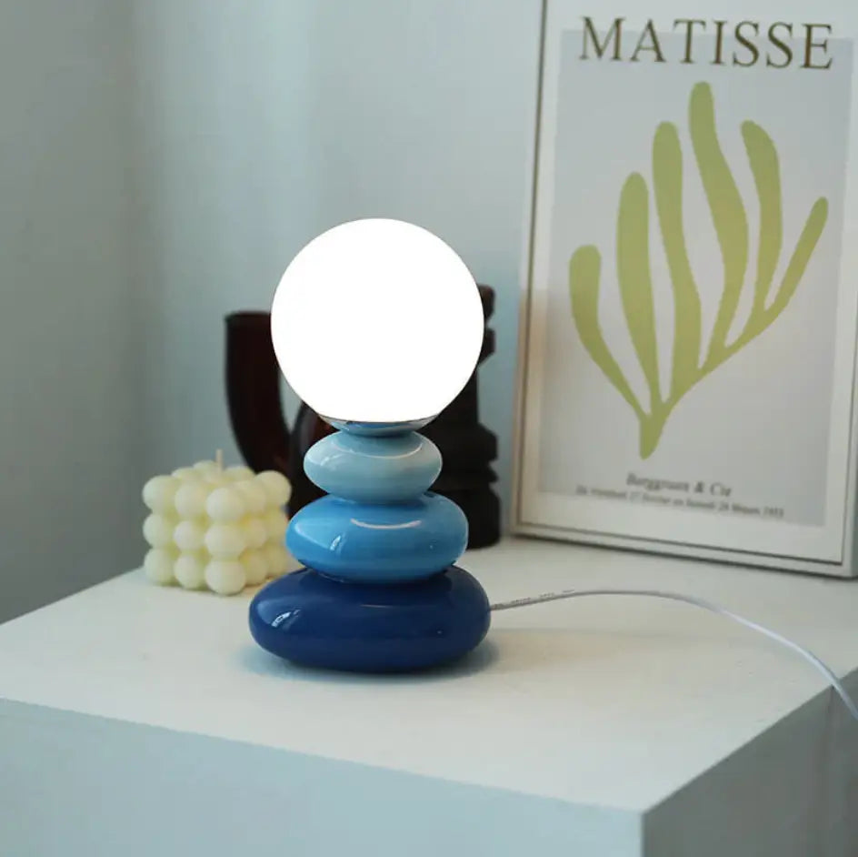 A modern bauhaus table lamp with tiered blue glass base and glowing white spherical bulb on top