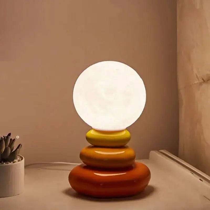 Warm glowing bauhaus table lamp with spherical shade and stacked glossy orange and yellow ring base for modern decor