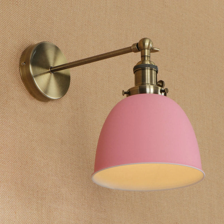 Pink dome-shaped wall sconce with brass accents and adjustable arm designed for bedroom lighting