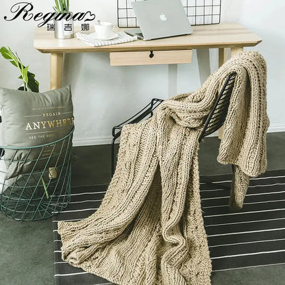 A decorbites beige chunky knit throw blanket with tassels draped over a black metal chair for cozy bedroom decor