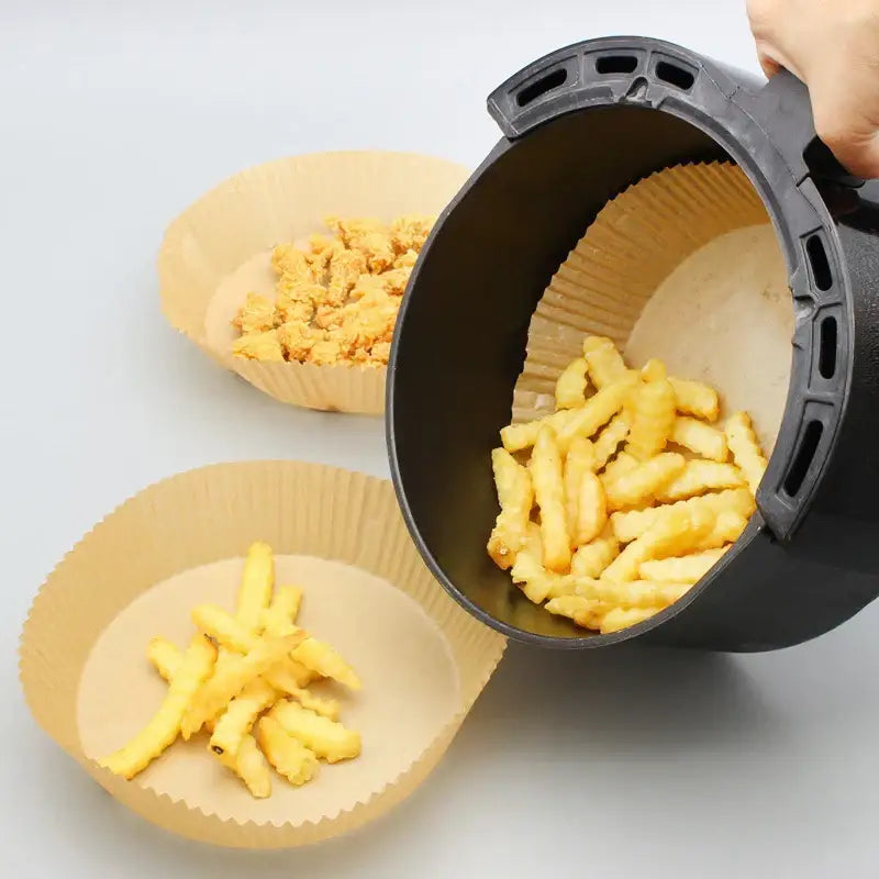 Black air fryer basket with ridged interior and handle grip shown alongside beige fluted decorbites air fryer paper liners 50pcs
