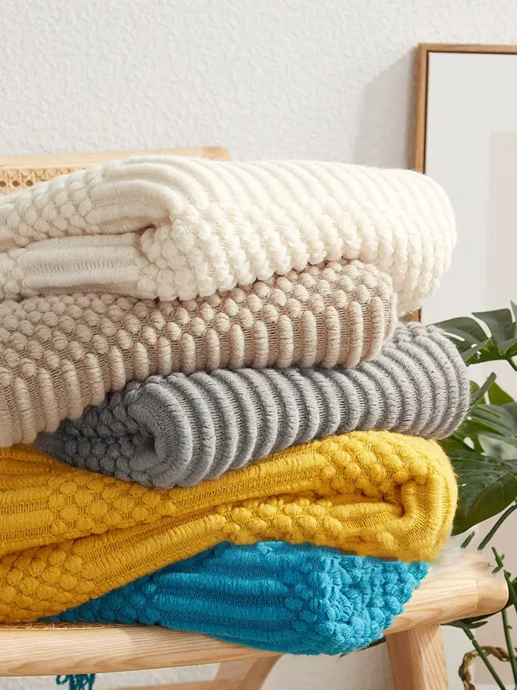 Stack of cozy cream beige gray yellow and blue sweaters with decorbites 3d knitted tassel blanket textures