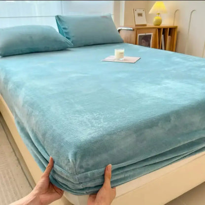 A soft light blue plush bedspread with cozy texture paired with a beige milk velvet fitted sheet for plush mattress topper
