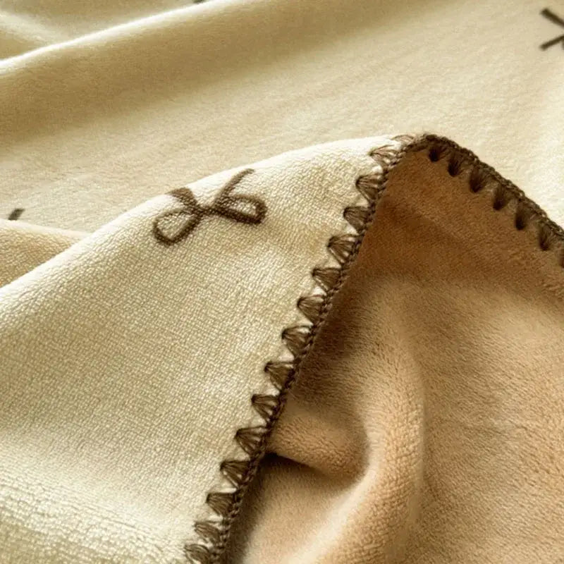 Beige scalloped cozy coral fleece blanket with cream plush side, brown embroidery, and zigzag stitched edge for decorbites cozy coral use