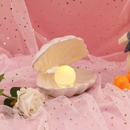 A soft pink decorbites ceramic shell pearl night light with a glowing yellow orb for bedroom decor