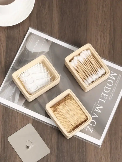 Three square light beige wooden containers holding cotton swabs and toothpicks complement a beige textured natural stone double decker jewelry organizer