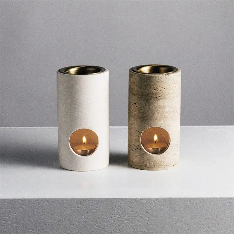 Two cylindrical concrete essential oil burner diffusers in smooth white and textured beige travertine stone with lit candles