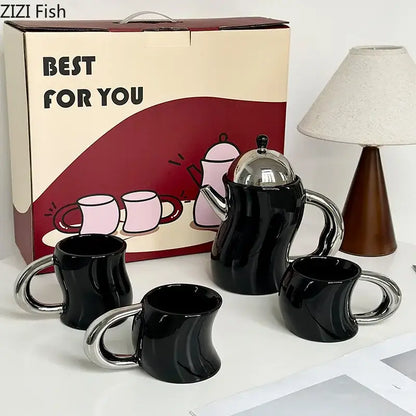 Black ceramic teapot with shiny silver lid and handle and three matching bending design ceramic coffee mugs with chrome handles