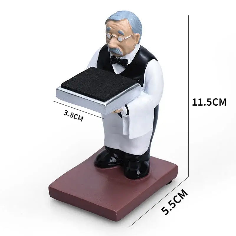 A miniature resin vintage waiter figurine holding a silver tray beside a black and iridescent purple cartoon bear watch stand