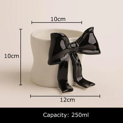 A white porcelain coffee cup with rounded edges and a glossy black bowknot accent for dining room use