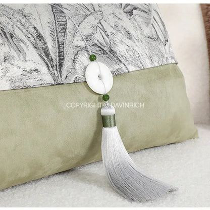 A delicate white tassel with jade-like beads hanging from a black and white green jungle plants pillow cover