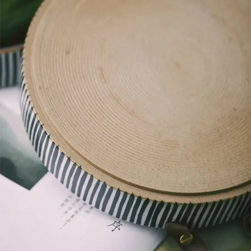 A light-colored wooden cutting board with visible grain and serrated edge next to a black and white striped porcelain bowl with leather handle decorbites porcelain bowl