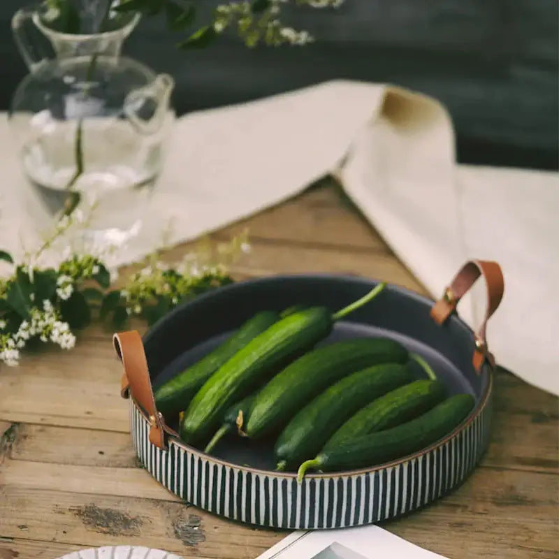 Round porcelain bowl with black and white stripes and brown leather handle holding fresh cucumbers decorbites porcelain bowl