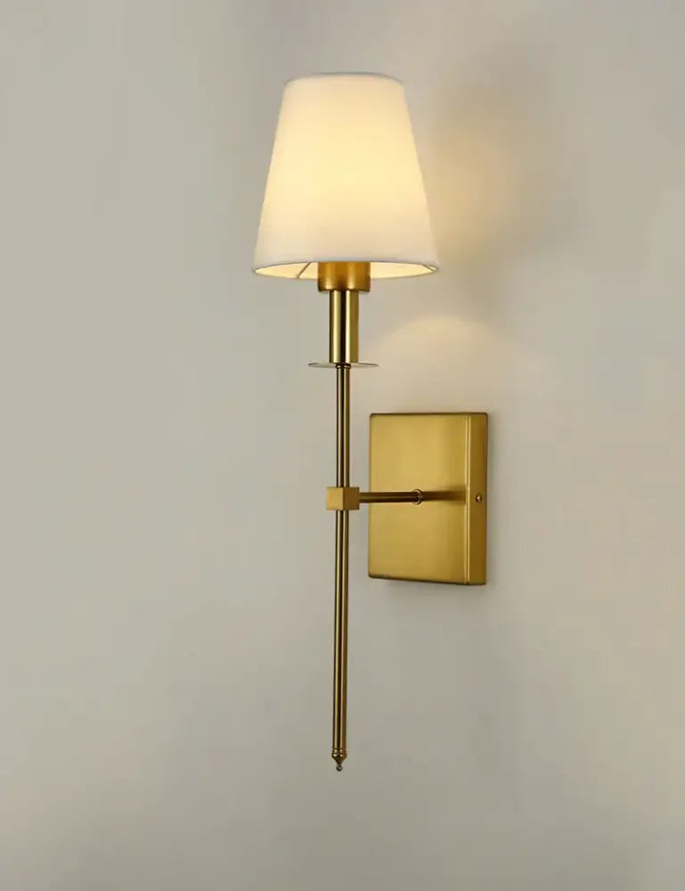Gold finished black brass wall sconce with a tapered white fabric shade for bedroom lighting