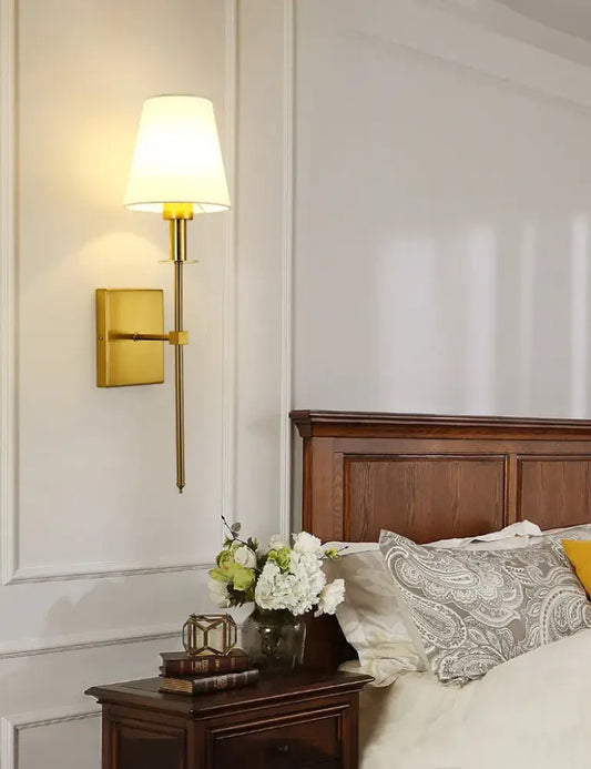 Gold-toned black brass wall sconce with tapered fabric shade for bedroom lighting