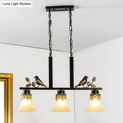 DecorBites black metal light pendant with gold bird and leaf details and three tan glass shades for dining room island