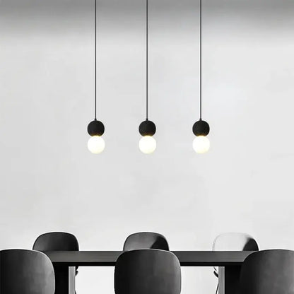 Three minimalist black travertine led pendant lights with spherical glass bulbs hang above a dining table decorbites black travertine