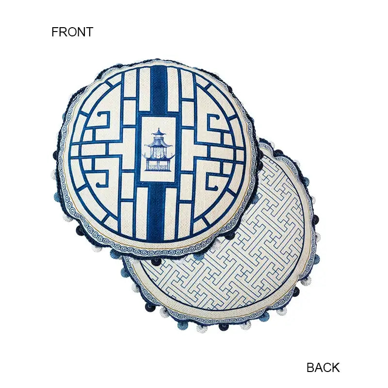 Circular cushion with blue chinoiserie home pagoda embroidered design framed by geometric patterns and dark pom-poms