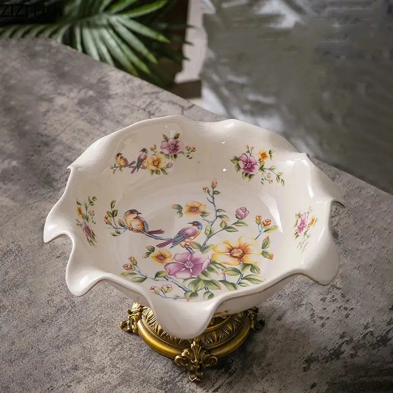 A delicate ivory flower pattern footed ceramic fruit bowl with decorbites blue flower motifs on a gold base stand