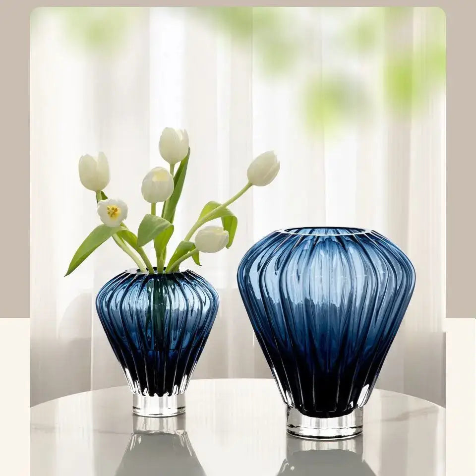 Two elegant blue glass hot air balloon vases with vertical ribbed texture and clear bases, one holding white tulips