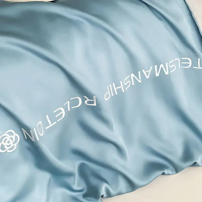 A light blue satin pillowcase with white embroidered text and floral logo in blue and gray cotton solid bedding set decorbites cotton solid color