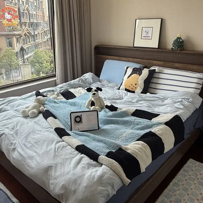A cozy bedroom decor featuring a flannel sofa blanket in blue green and black stripes with plush pillows and stuffed animals