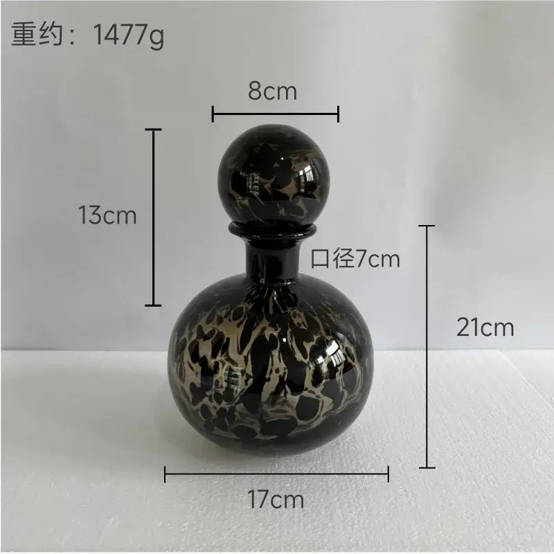A glossy black glass perfume bottle with swirling gold patterns and spherical stopper for decorbites leopard print decor