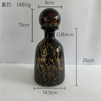 A glossy black glass decanter with swirling gold and brown marbled patterns and a spherical stopper decorbites leopard print decor