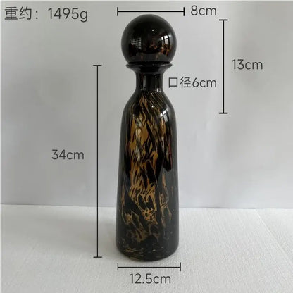 A tall glossy black glass decanter with swirling amber and gold marbled patterns and spherical cap decorbites leopard print