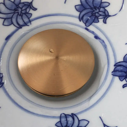 Blue and white porcelain basin set with pop drain featuring a circular brushed brass disc with radial texture and droplet