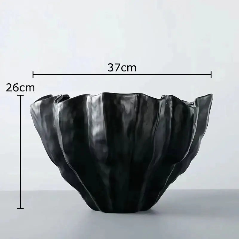Black ceramic bowl with sculpted petal-like rim and glossy finish displayed alongside white porcelain jar with gold plating for living room decor